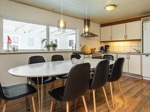 A modern kitchen with a dining area, featuring a white table, black chairs, and wooden flooring. - 4 Star Holiday Home in Vejers Strand (Vejers Strand)