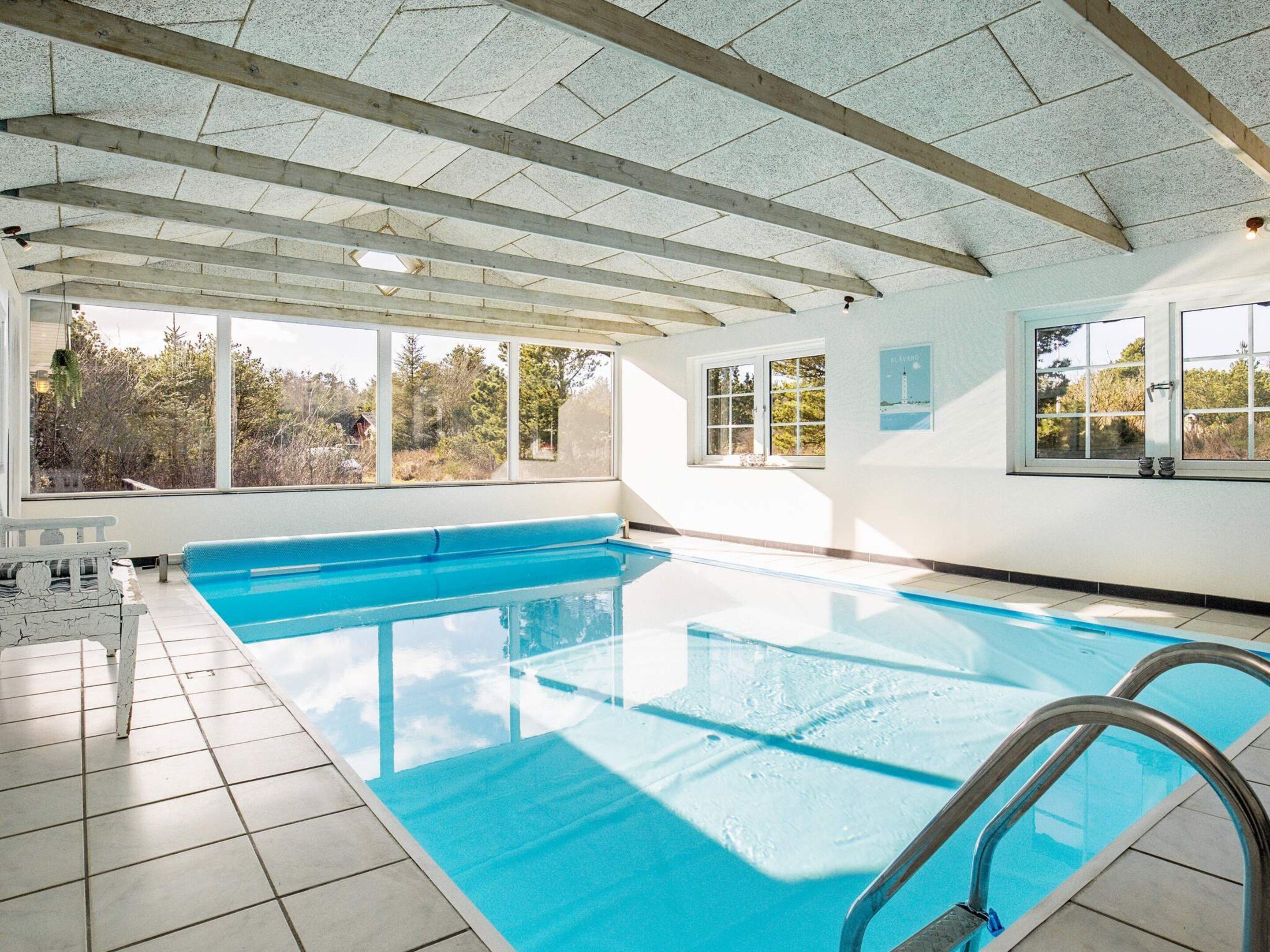 En indendørs swimmingpool med frit udsyn til omgivelserne gennem store vinduer.