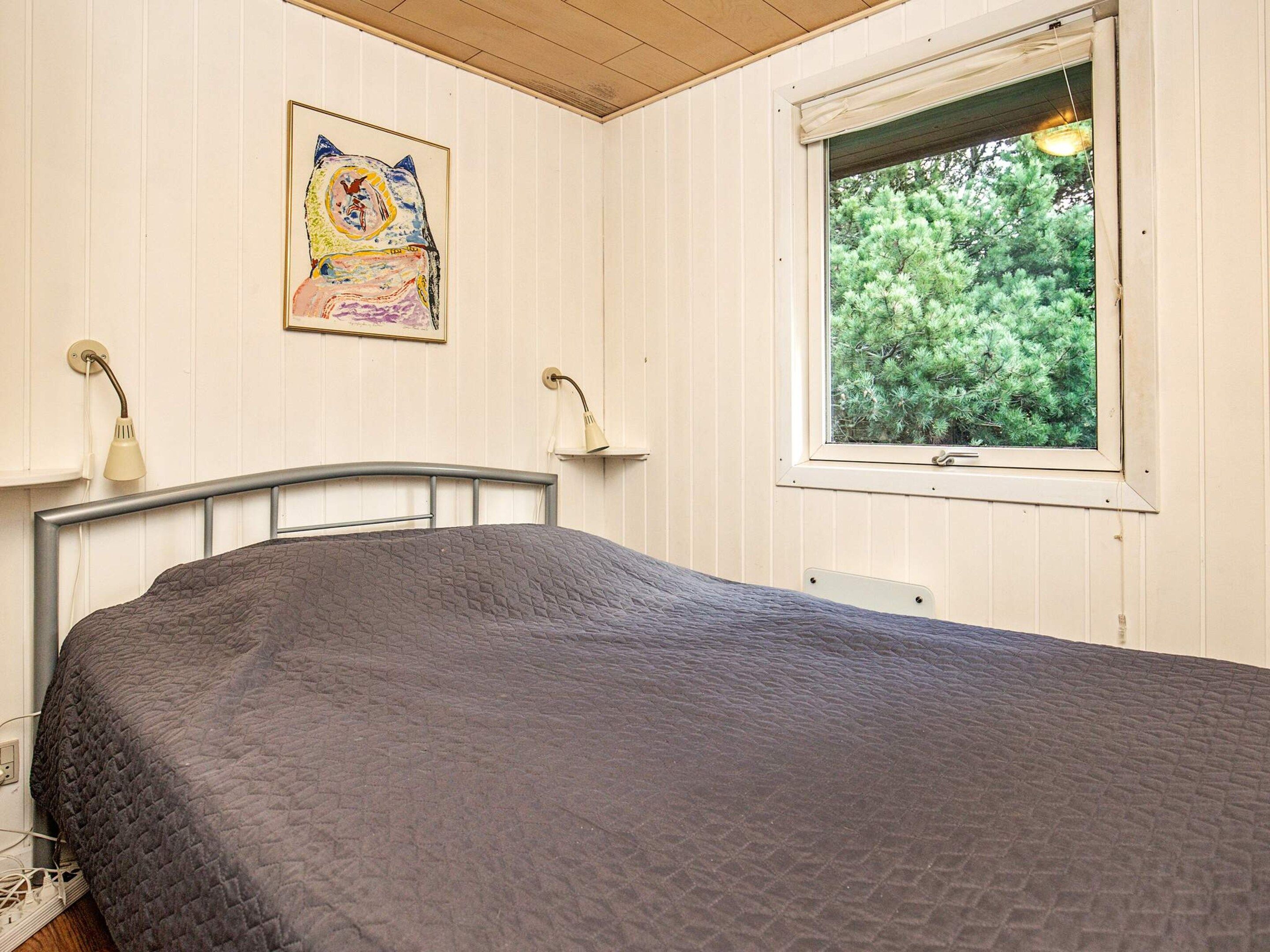 A bedroom with a bed, a window with a view of trees, and a wall-mounted lamp.
