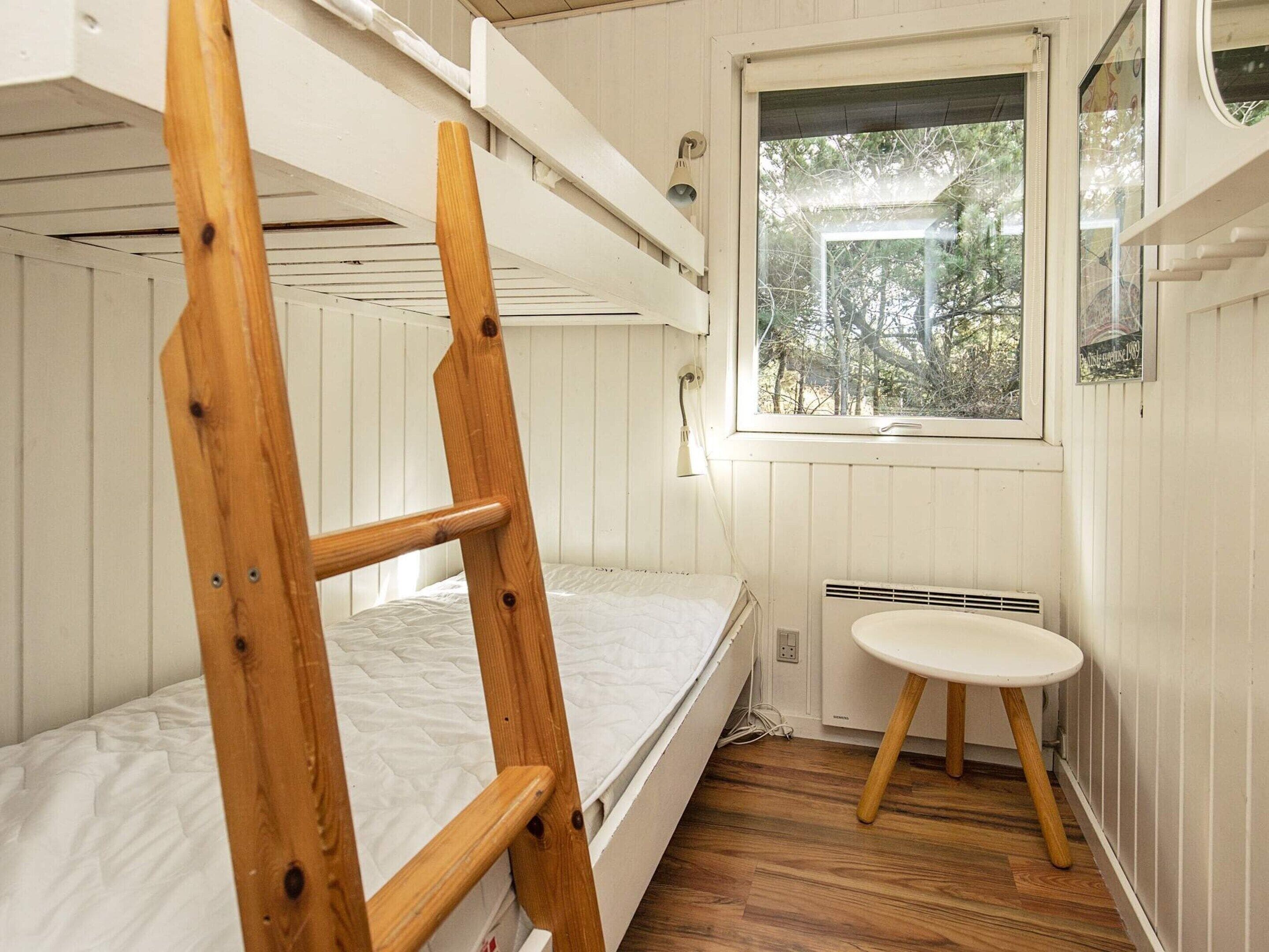 Camera con letto a castello, una scala in legno, un comodino e una finestra con vista sugli alberi.