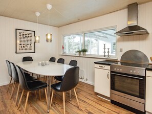 A kitchen with a round dining table, black chairs, a stainless steel stove, and a window with a view of the outdoors. - 4 Star Holiday Home in Vejers Strand (Vejers Strand)