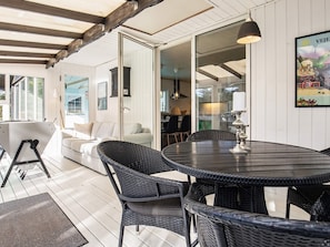 A dining area with a round table and wicker chairs, a sofa, and a pendant light. - 4 Star Holiday Home in Vejers Strand (Vejers Strand)