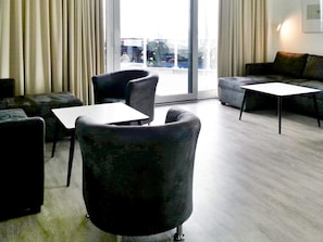 A modern living room with a sofa, two armchairs, a coffee table, and a view of the city through large windows. - Holiday Home in Wendtorf (Wendtorf)