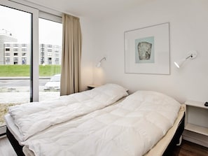 A hotel room with a bed, a window with curtains, a wall-mounted lamp, and a framed picture.