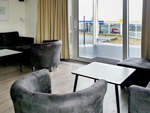 Decoração moderna com assentos estofados em cinza, uma mesa branca e uma grande porta de vidro que dá para uma área externa.