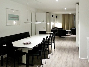 A modern dining area with a white table, black chairs, and pendant lighting.