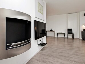 Uma sala de estar moderna com uma TV curva fixada na parede, uma TV de tela plana, uma mesinha com uma cadeira e um radiador.