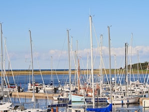 A marina with multiple sailboats docked, a wooden pier, and a clear view of the water and distant land. - Holiday Home in Wendtorf (Wendtorf)
