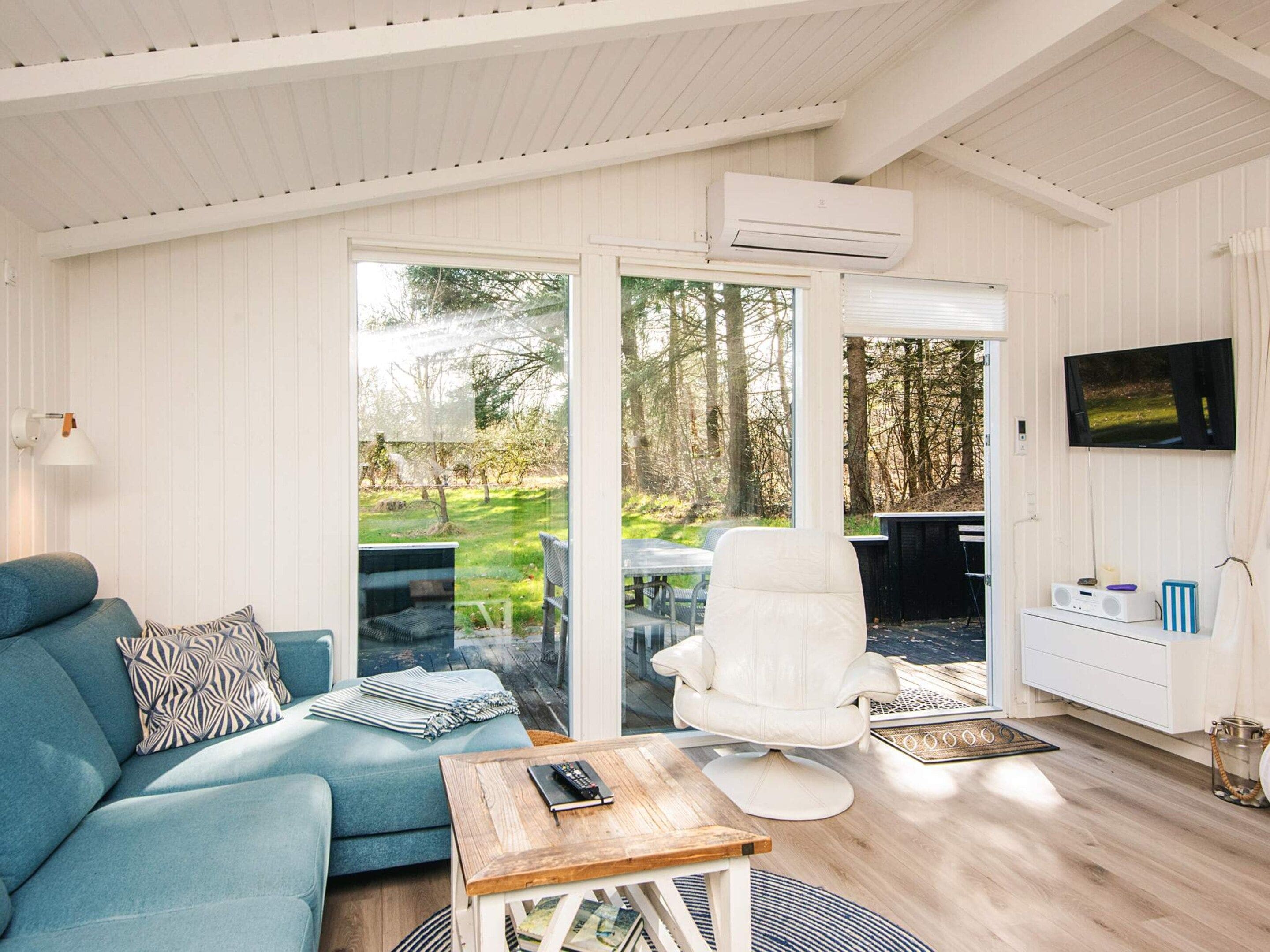 Una sala moderna con un sofá azul, un sillón blanco, una mesa de centro y un televisor montado en la pared.
