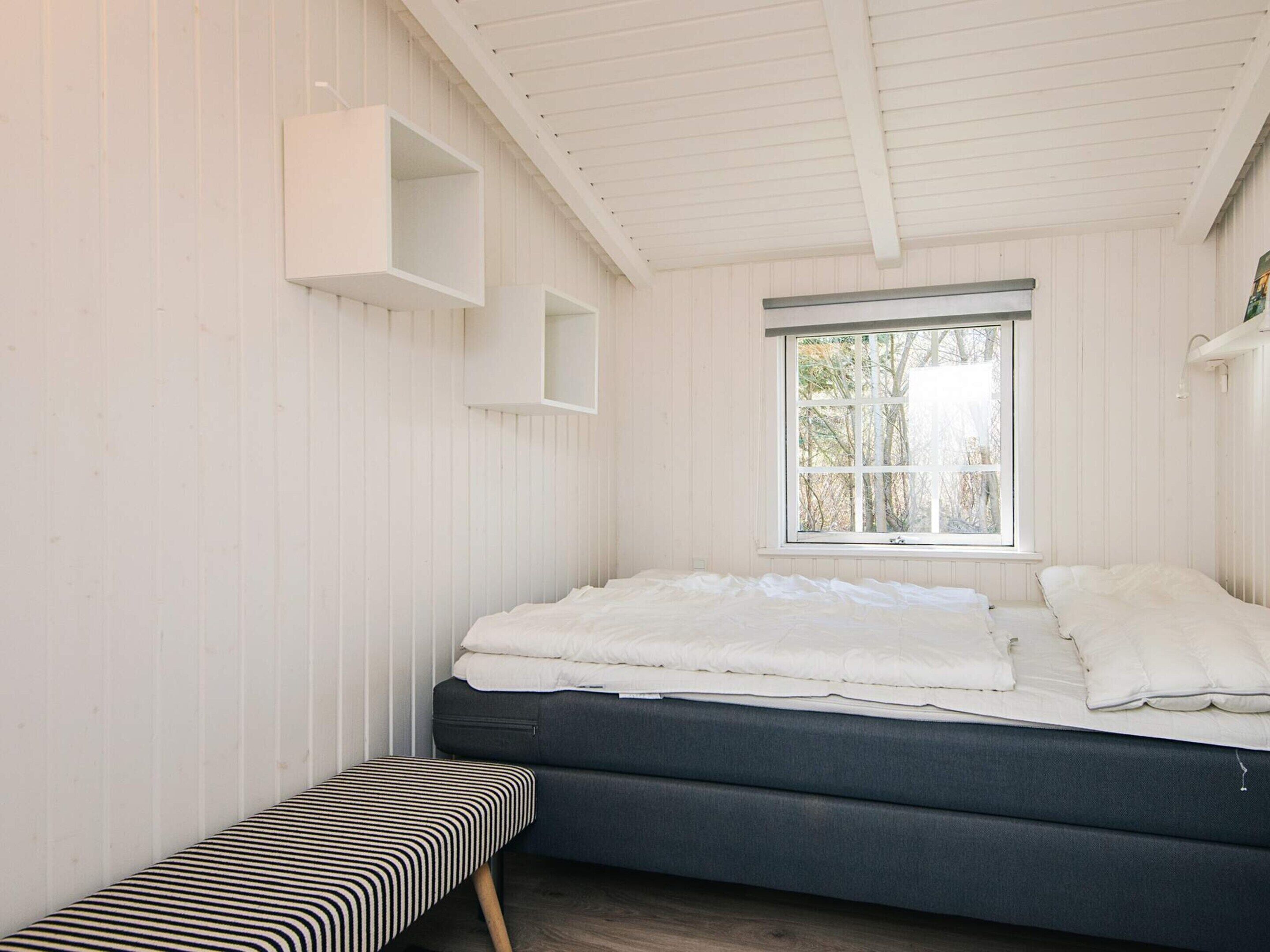A bedroom with a bed, a bench, and a window with a view of trees.