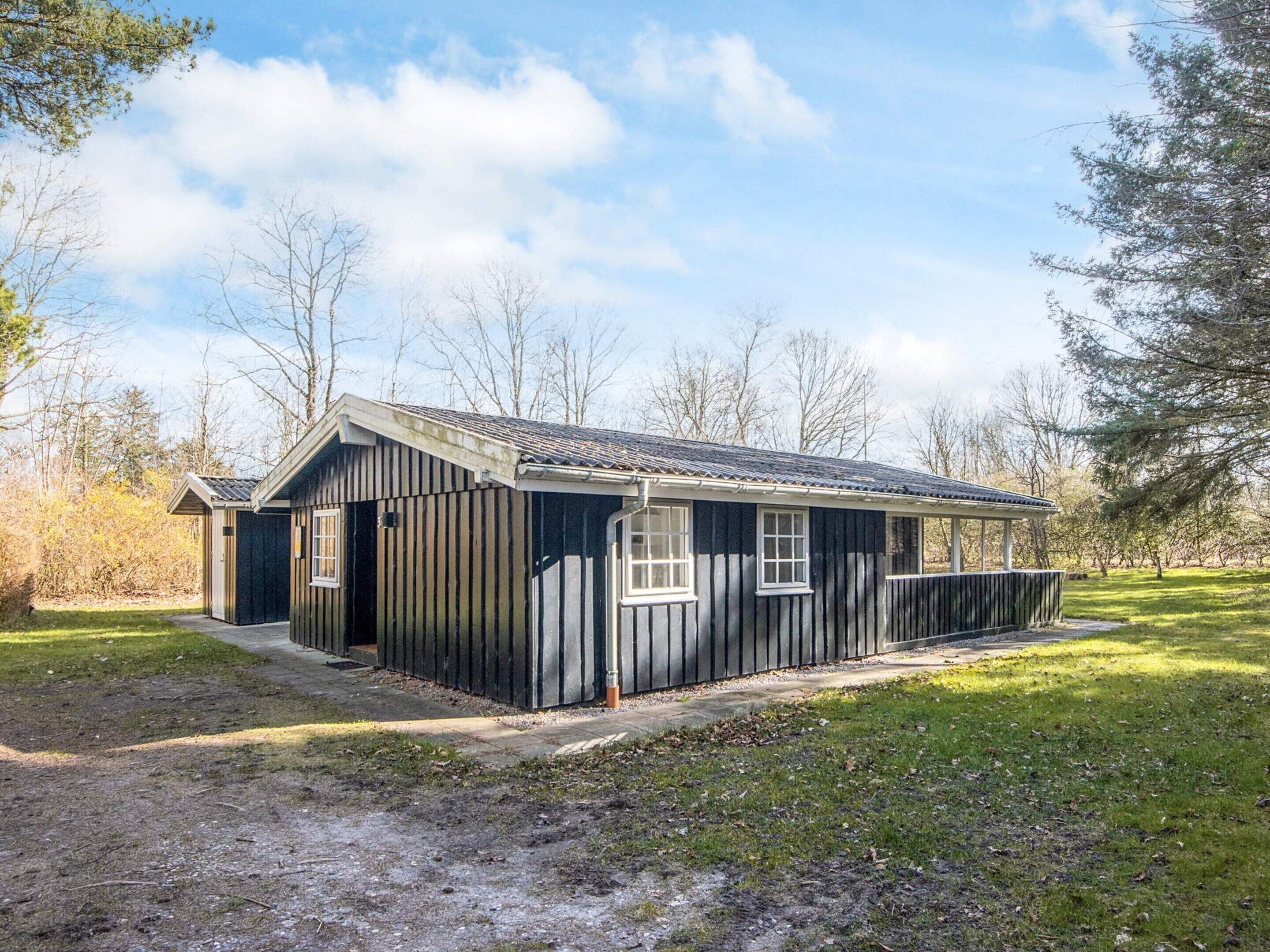 A small, single-story wooden cabin with a gabled roof, a front porch, and a fenced yard.