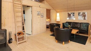 Een gezellig houten blokhutinterieur met een slaapzolder, een open haard, een bank en een eethoek.