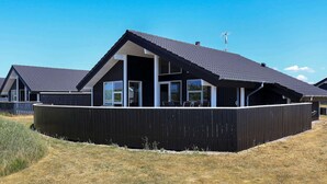 Een modern huis met een donkere gevel, grote ramen en een schuin dak.