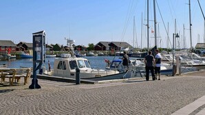 Een jachthaven met aangemeerde boten, een houten bankje en een rij gebouwen op de achtergrond.