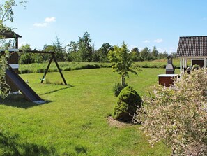 Une cour verdoyante avec une balançoire, un petit arbre et un barbecue.