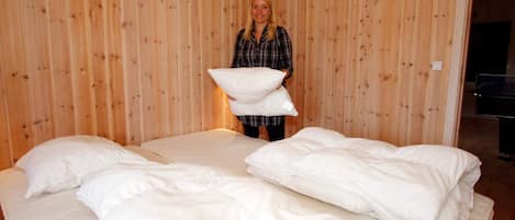 A room with wooden panel walls, a bed with white bedding, and a person holding pillows.