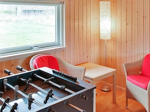 Una habitación con mesa de fútbol, sillas de mimbre, una mesa y una lámpara frente a una pared de madera.