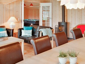 A cozy room with a pool table, leather chairs, a dining table, and a wood-burning stove.