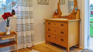 A room with a wooden dresser, a mirror, a vase with flowers, a striped curtain, and a rug.