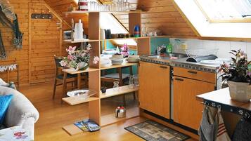 A cozy, well-organized kitchen with wooden cabinets, a dining area with a table and chairs, and a lofted sleeping area with a bed.