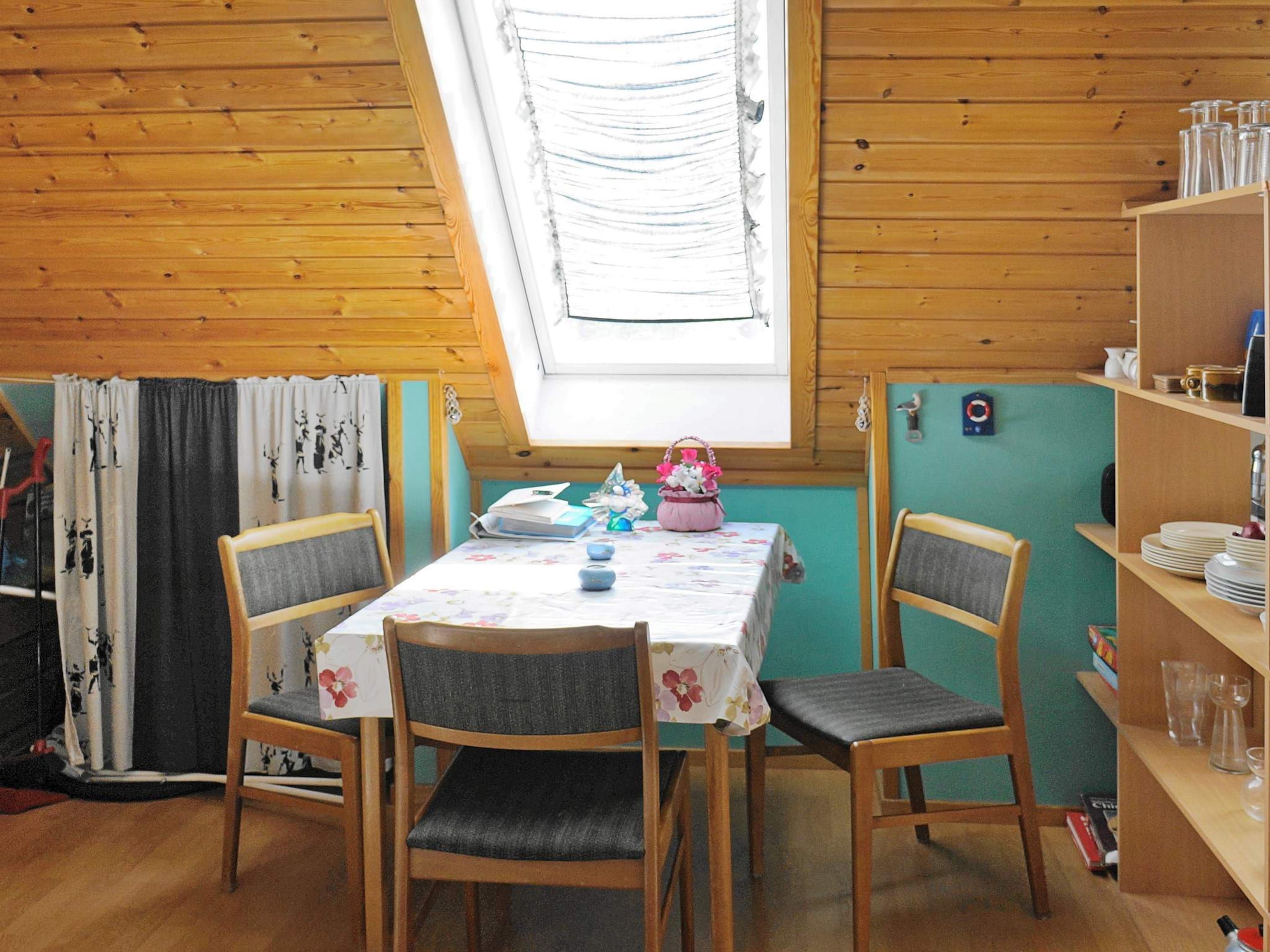 Une pièce chaleureuse avec un plafond en bois, une lucarne, une table avec des chaises et une bibliothèque.