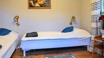 A room with two beds, a painting on the wall, and a window with curtains.