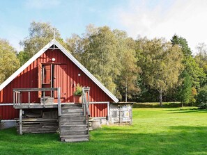 Punainen lato, jonka puinen portaikko johtaa kuistille. Ladon ympärillä on vihreää ruohoa ja puita.