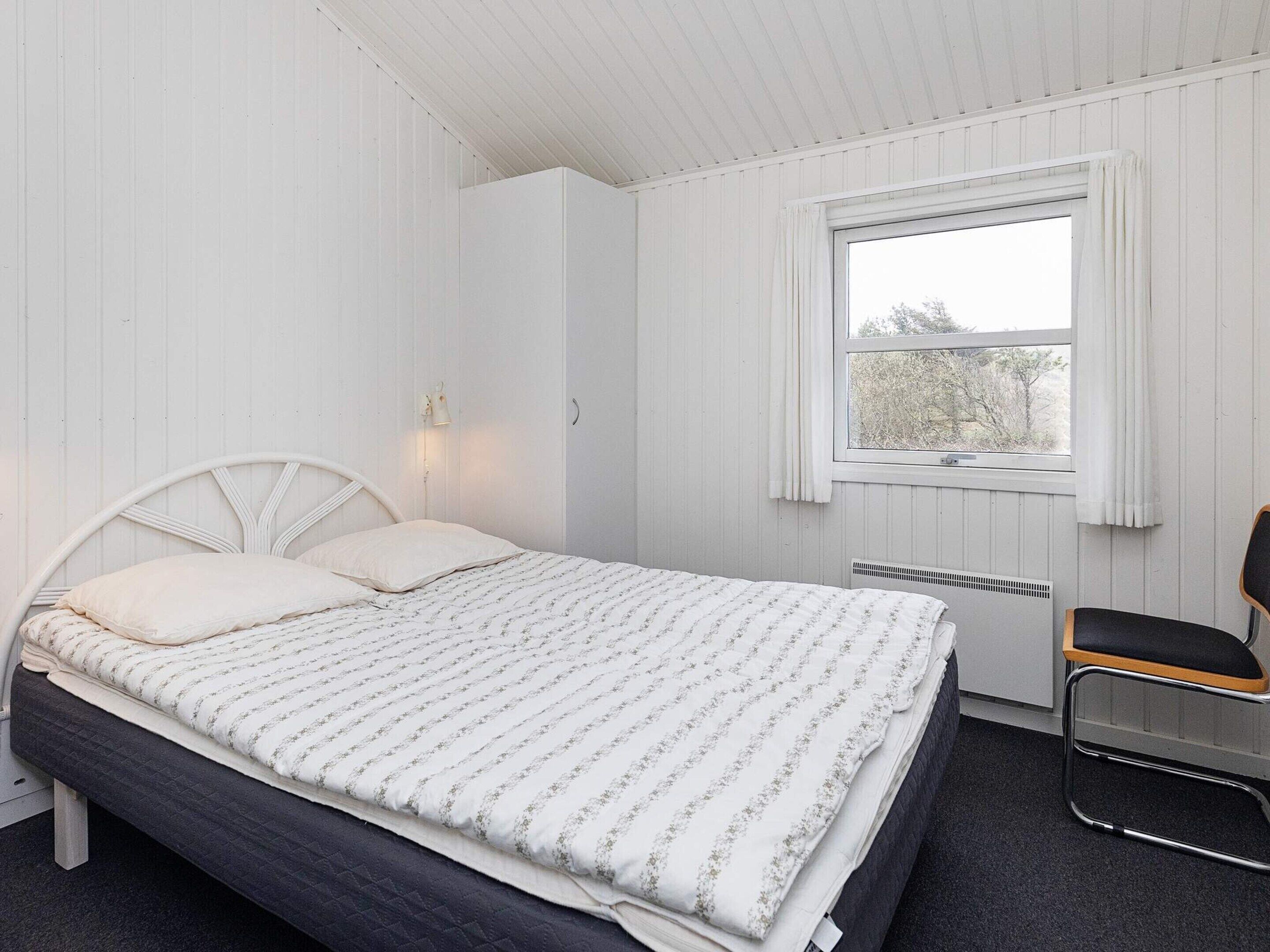 A bedroom with a bed, a window with curtains, a radiator, and a chair.