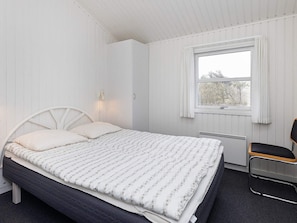 A bedroom with a bed, a window with curtains, a radiator, and a chair.
