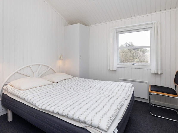 A bedroom with a bed, a window with curtains, a radiator, and a chair.