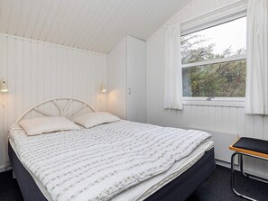 Une chambre à coucher avec un lit, une fenêtre avec des rideaux, une lampe de chevet et un petit banc.