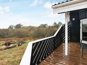 A wooden deck with a black railing, a glass door, and a view of a natural landscape.