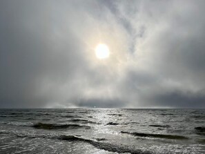 A stormy sea with waves and a sun partially obscured by clouds.
