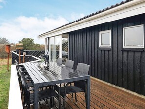 En terrasse med et bord og stole, et træhegn og en klar himmel.