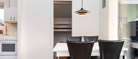 Een moderne keuken met witte kasten, een fornuis en een eethoek met een witte tafel en zwarte stoelen.