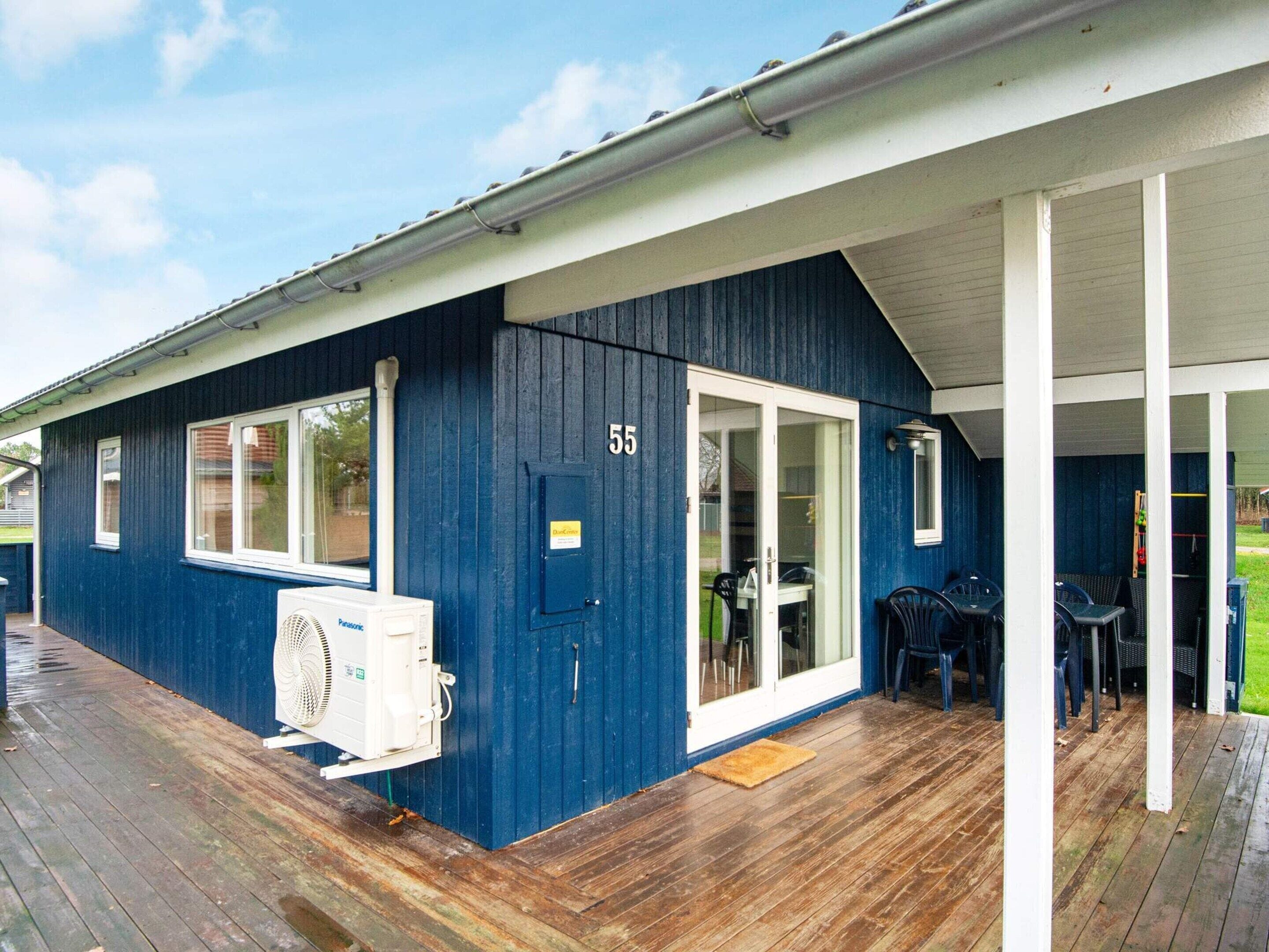A blue building with a number '55' on the door, a covered porch with chairs, and a white air conditioning unit.