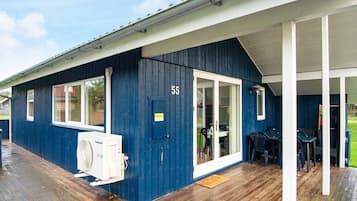 A blue building with a number '55' on the door, a covered porch with chairs, and a white air conditioning unit.