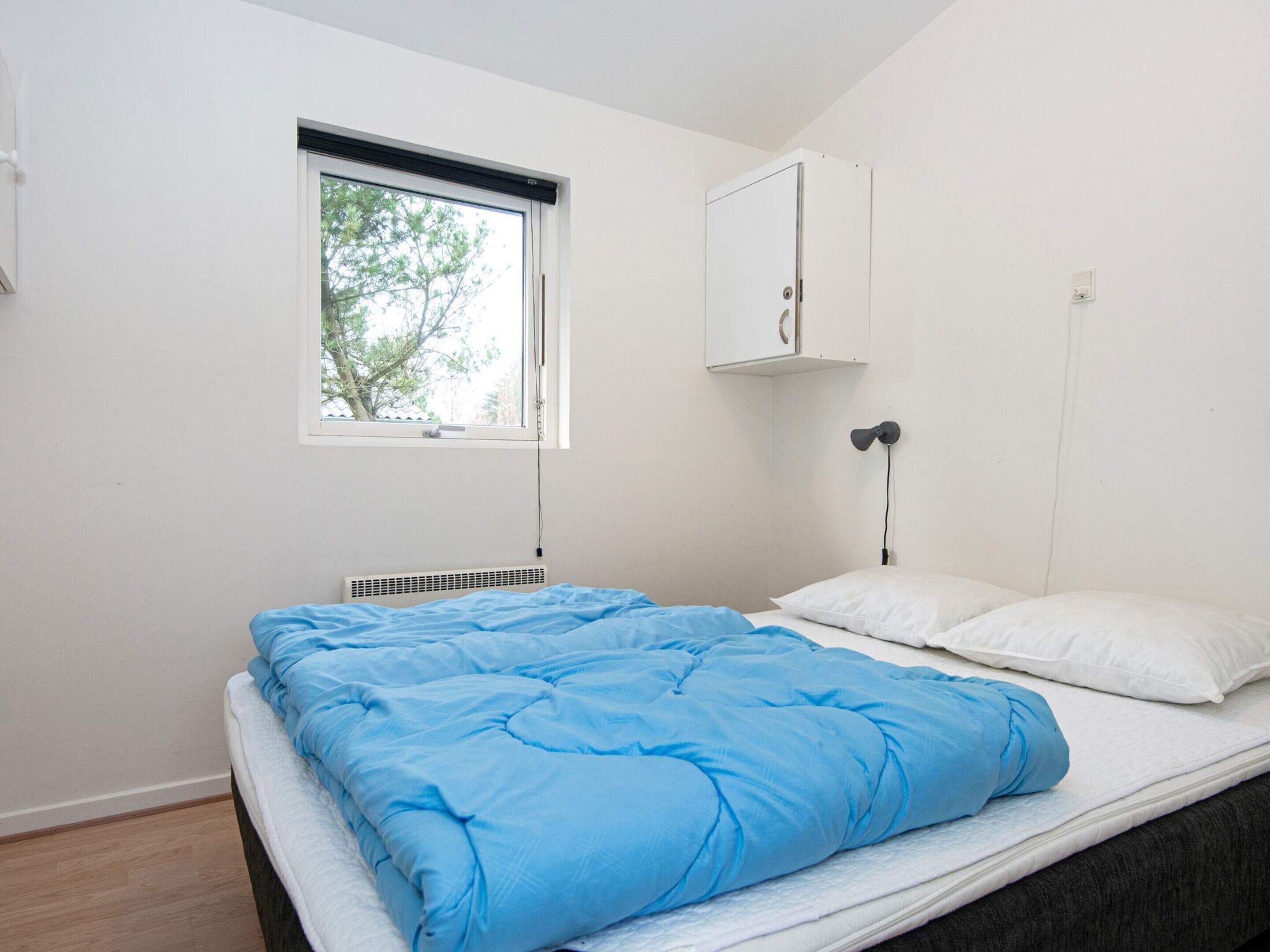 A bedroom with a single bed, a window, a radiator, and a wall-mounted cabinet.