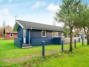 A single-story building with a sloped roof, a fenced yard, and a tree in front. - 4 Person Holiday Home in Hovborg (Hovborg)