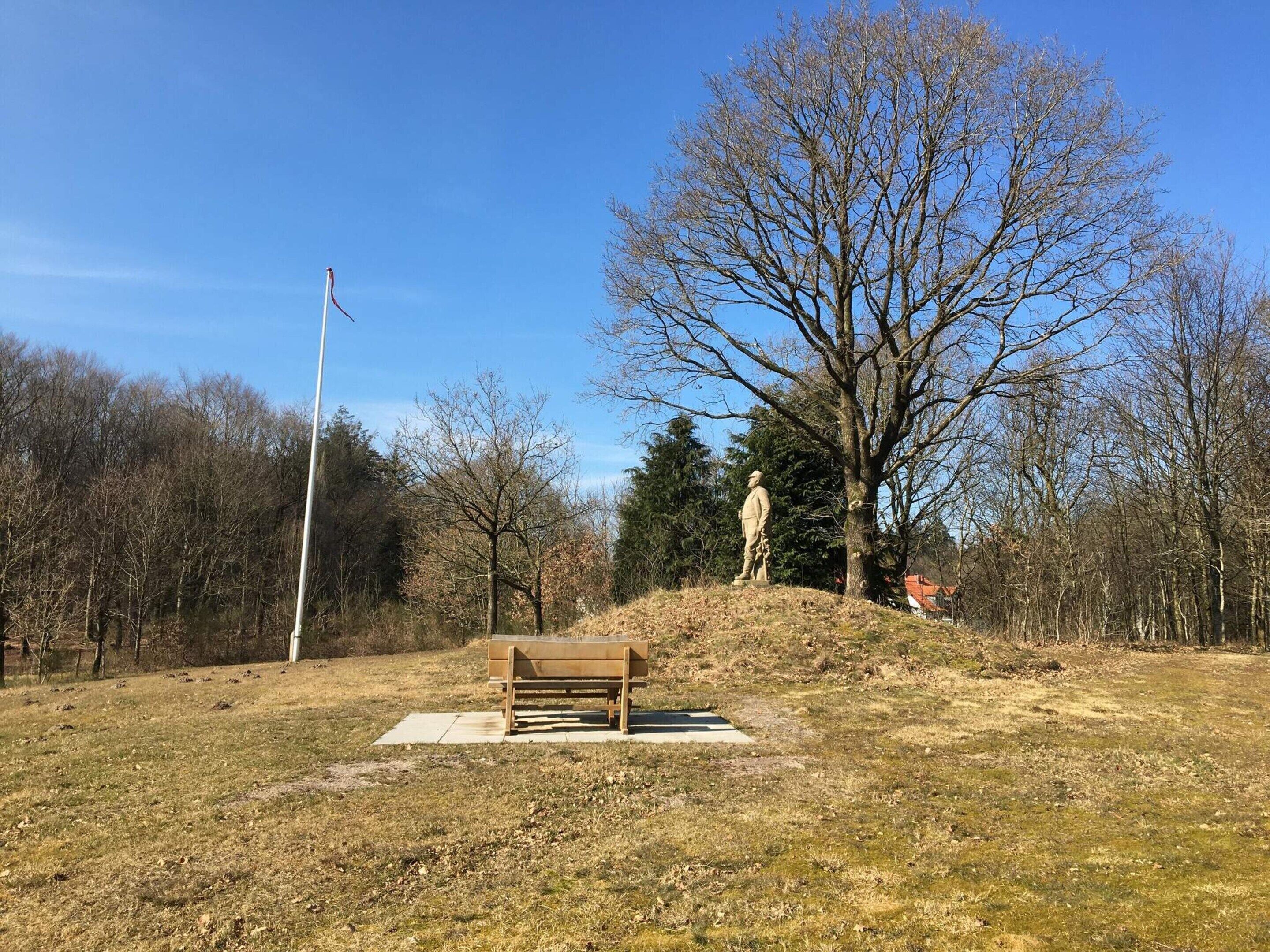 A park with a wooden bench, a statue, and a flagpole.