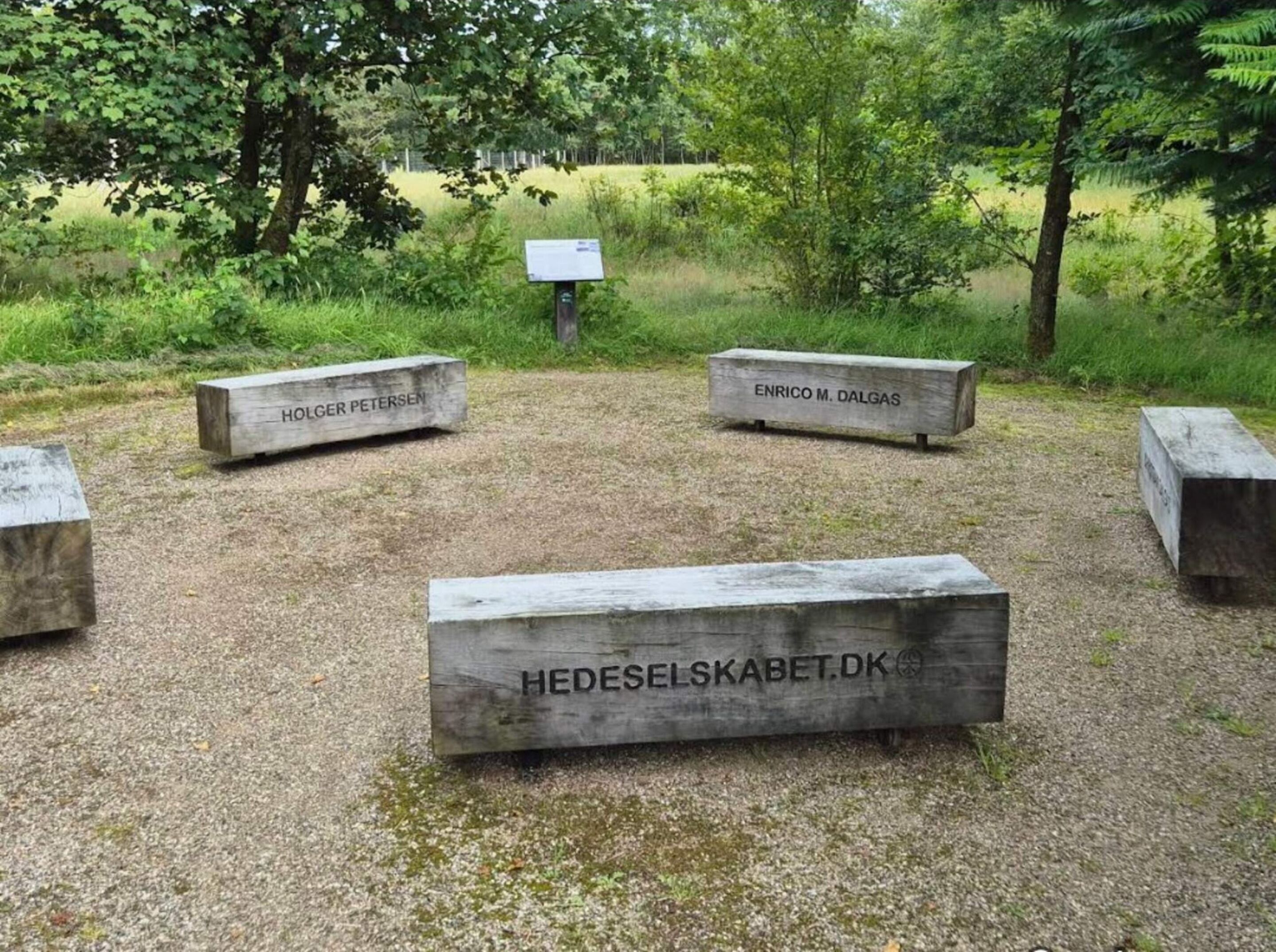A memorial with engraved names on wooden benches in a grassy area surrounded by trees.