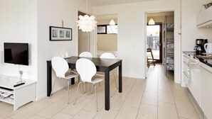 A modern kitchen with white cabinets, a coffee machine, and a dining area with a dark table and white chairs.