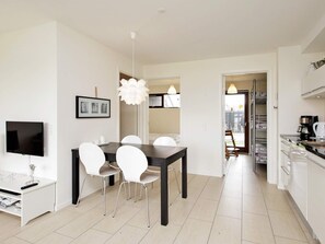 A modern kitchen with white cabinets, a coffee machine, and a dining area with a dark table and white chairs.