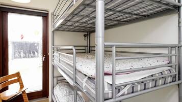 A bunk bed with metal railings and a wooden chair in a room with a tiled floor.