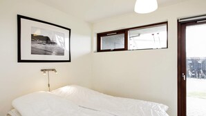 A bedroom with a bed, a framed picture, a window, and a door.