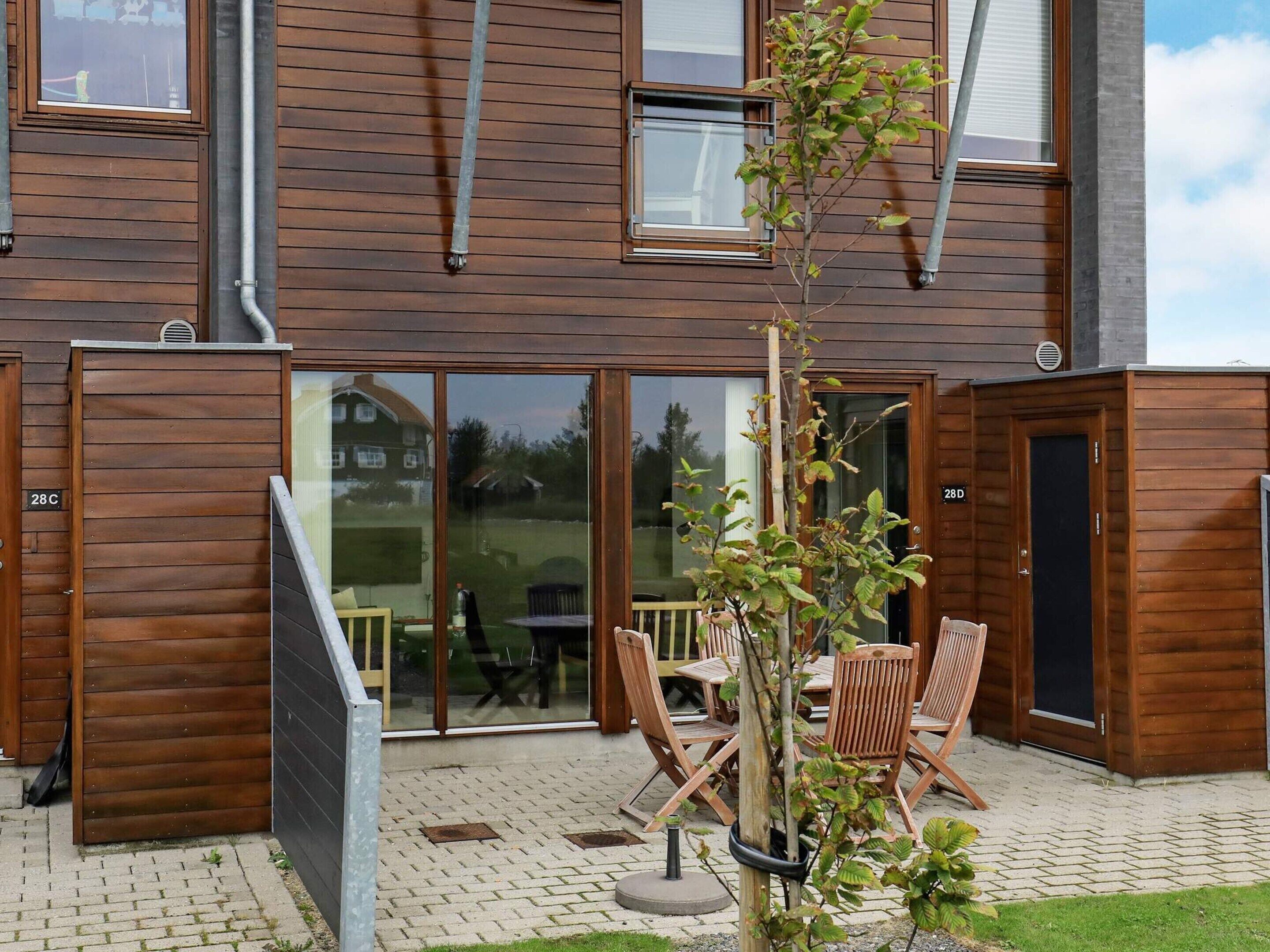 A modern building with wooden siding, large sliding glass doors, and a small patio area with outdoor furniture.