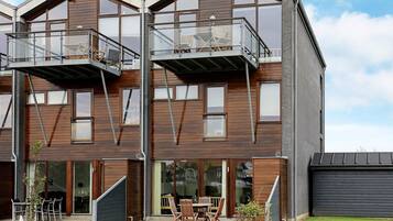 A modern multi-story building with balconies, large windows, and a patio area with outdoor furniture.