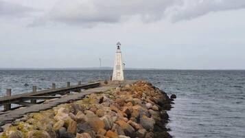 A lighthouse on a rocky pier extending into the sea, with a cloudy sky overhead.