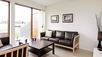 A modern living room with a leather sofa, a coffee table, and a view of a residential area through large windows.