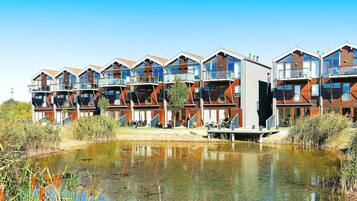 A modern multi-story residential building with balconies, a small pond in front, and surrounding vegetation.